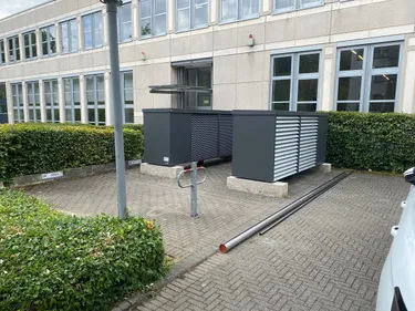 Ein weißer Van parkt vor einem Gebäude mit Wärmepumpen.