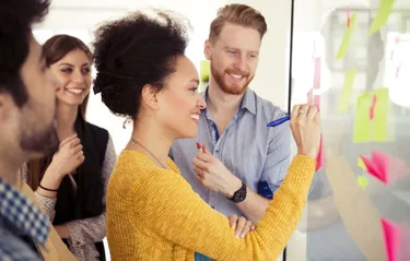 Eine Gruppe von Personen steht um ein Whiteboard und diskutiert gemeinsam Ideen und Konzepte.