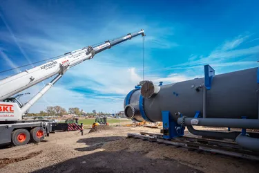 Schwelastkran hebt Verdampfer auf Schienen vor Halle